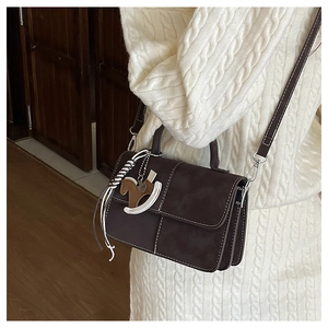 Detail of a dark brown crossbody square bag with white stitching and wooden horse charm