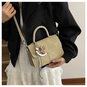 Beige crossbody bag with horse charm detail shown on model in a stylish street setting
