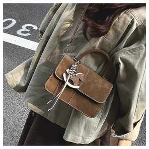 Detail view of brown suede crossbody bag with trojan horse pendant on street background