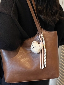 Brown leather tote bag with a cute plush bear charm and stylish braided strap detail