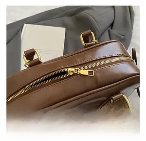 Détail des fermetures éclair métalliques et de la boucle dorée sur un sac en cuir marron
