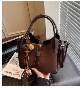 Detail of a brown patchwork handbag with metal twist lock and decorative tassel charm