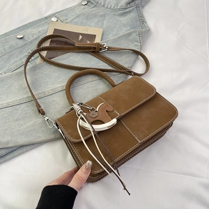 Close-up of brown suede crossbody bag with decorative rocking horse charm and white stitching
