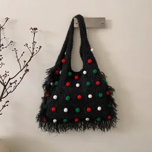 Détail d'un sac en tricot noir avec pompons colorés et longues franges sur le côté