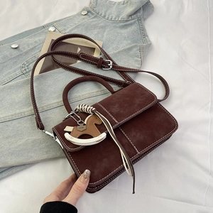 Detail of dark brown suede handbag featuring white contrast stitching and wooden horse charm