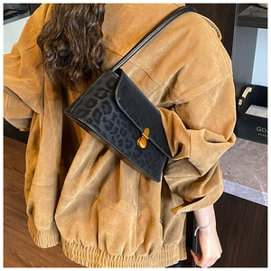 Detail of black leopard print underarm bag with gold metal clasp on corduroy jacket