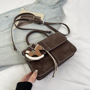 Detail of dark brown suede handbag with white stitching and rocking horse charm