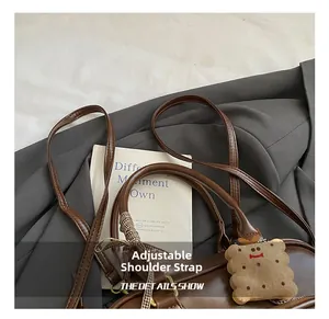 Détail du sac rétro marron montrant la bandoulière réglable et le pendentif mignon