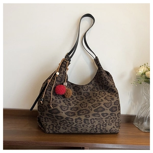 Detail of leopard print tote bag with plush pompom charms on a wooden shelf