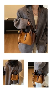 Detail view of suede bucket bag featuring metallic twist lock and decorative tassel charm