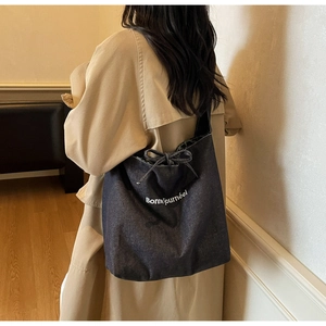 Détail du sac cabas en denim bleu avec imprimé français blanc et nœud décoratif à cordon