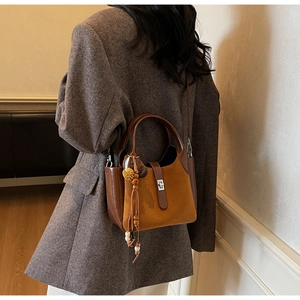 Detail view of two-tone brown bucket bag with bohemian fringe tassel and metal lock
