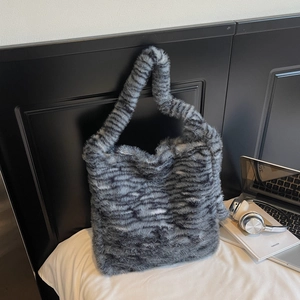 Close-up of a soft grey striped faux fur tote bag resting on white bedding decor