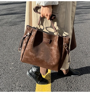 Deep brown suede tote bag with golden ring hardware and rivets shown in street style