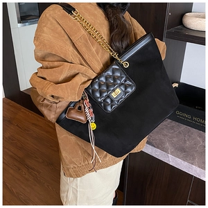 Close-up of black tote bag featuring gold chain strap and quilted pocket with charms