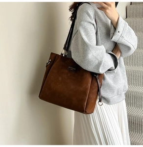 Detail view of a large brown suede tote bag styled with casual outfit in soft indoor light