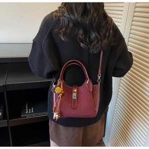Detail of burgundy bucket bag with ethnic tassel charm and suede-leather texture mix