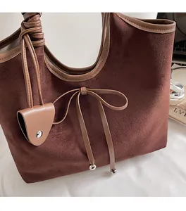 Close-up of brown suede tote bag featuring a leather bow knot and metal ball charms