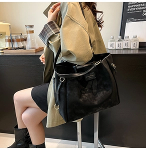 Detail of matte black leather tote bag featuring golden hardware and adjustable strap