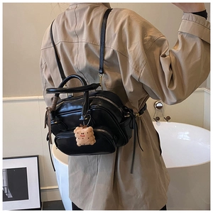 Détail d'un sac à dos noir en similicuir avec plusieurs poches zippées et breloque ours
