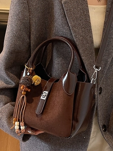 Brown vintage suede bucket bag with metal lock and decorative tassel on a suit jacket