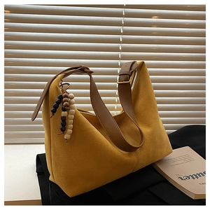 Detail of mustard yellow suede tote bag with brown leather strap and wooden bead charm