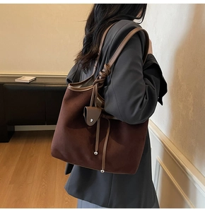 Brown suede tote bag detail featuring knotted handle and leather charm on gray blazer