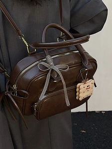 Sac Boston vintage marron avec ruban à carreaux et breloque peluche présenté par un modèle