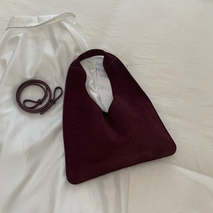 Detailed close-up of a burgundy suede shoulder bag with a matching adjustable strap