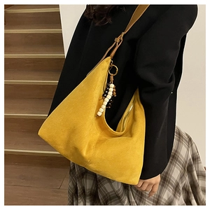 Detail view of yellow faux suede hobo bag with colorful beaded charm on a shoulder strap