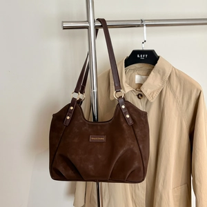 Dettaglio della borsa in pelle scamosciata marrone scuro con anelli dorati e logo