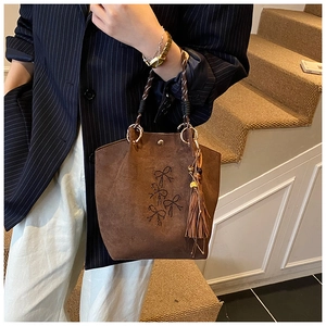 Detail van karamel suède handtas met geborduurd strikmotief en bohemien kwastje hanger