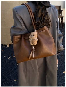 Detail of large brown suede-like tote bag with plush bear charm and thin straps