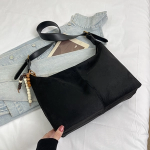 Detailed close-up of a black suede handbag featuring a stylish beaded charm accessory