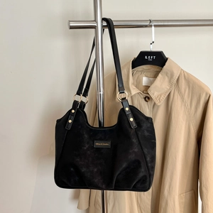 Dettaglio della borsa tote nera opaca con anelli dorati e un'etichetta in pelle minimalista