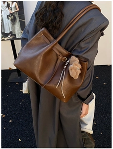 Brown vintage suede tote bag with plush bear charm worn on shoulder for daily commute