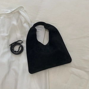 Detail view of black suede tote bag with integrated handle and detachable leather shoulder strap