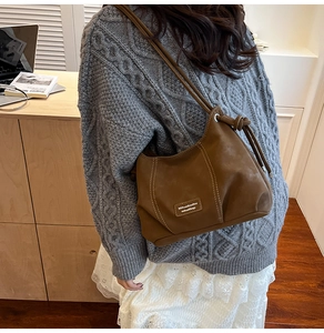 Detail showing caramel brown suede shoulder bag worn with a grey cable knit sweater