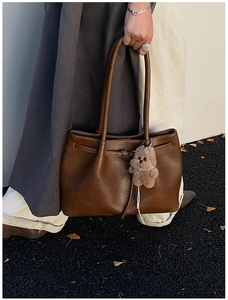 Detail of deep brown suede tote bag featuring a leather knot and plush puppy charm
