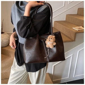 Detail of dark brown faux suede tote bag with golden buckle and plush bear pendant
