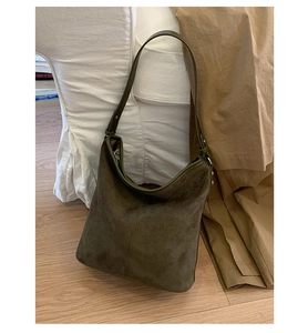 Detail of olive green suede tote bag with decorative stitching on white sofa