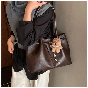 Detail of dark brown faux leather tote bag with slender straps and cute plush bear charm