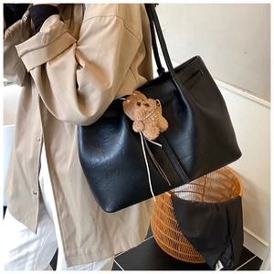 Detail of black PU leather tote bag with brown bear charm on beige trench coat outfit