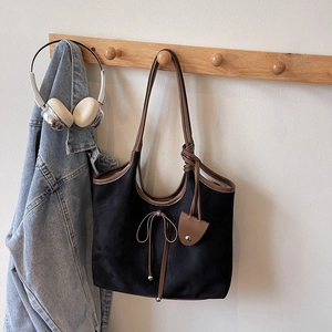 Detail of black suede tote bag featuring a leather bow knot and brown decorative hangtag