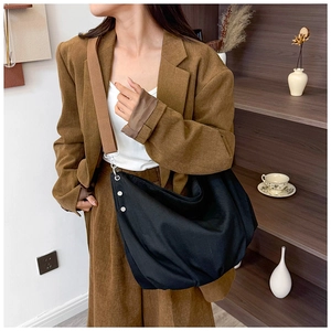 Detail view of large black canvas hobo bag with wide brown strap on model outfit