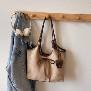 Detail of khaki frosted tote bag with bow accent and brown leather trim on wall hook