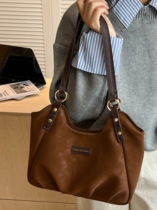 Borsa a spalla in pelle smerigliata marrone con anelli dorati indossata da modella