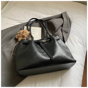 Close-up of black suede tote bag featuring a golden square buckle and cute brown bear charm