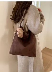 Détails de la texture du sac hobo en daim marron avec petit ours en peluche et pompon chic