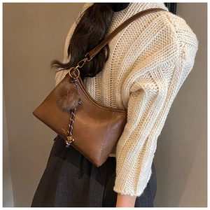 Detailansicht der braunen Retro-Schultertasche mit Plüschball-Anhänger auf weißem Strick